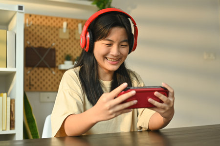 Joyful teenage asian girl playing video game on a portable game console at home. Leisure, entertainment and technology.の写真素材