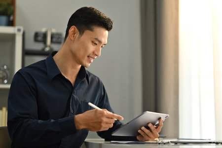 Attractive male marketing business manager sitting in modern office and using digital tablet. Business technologies concept.の写真素材