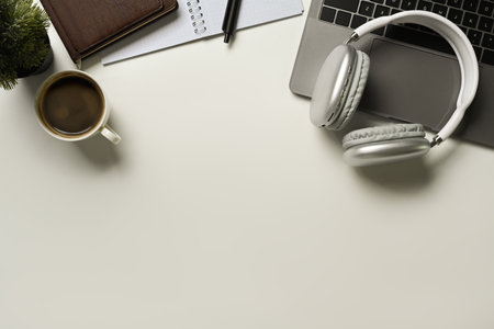 Top view of laptop, headphone, empty notepad and coffee cup on white table. Copy space for your...