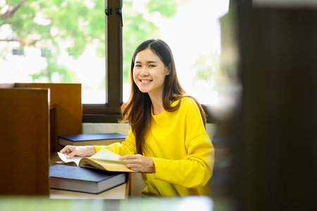 Cheerful young asian female student doing class assignment, reading book in library. University, education and lifestyle.の写真素材