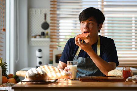 Portrait of handsome asian man eating a fresh slice of bread with jam for breakfast.の写真素材