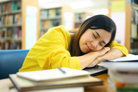Tired asian female student taking a nap in the university library during preparing for exams.の写真素材