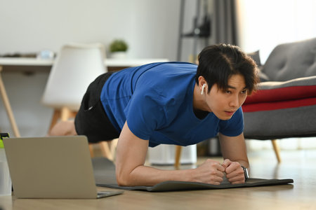 Fit athletic man doing plank position while exercising in cozy home interior. Healthy lifestyle and sport concept.の写真素材
