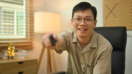 Casual man in glasses holding remote control, watching TV on the couch at home.の写真素材