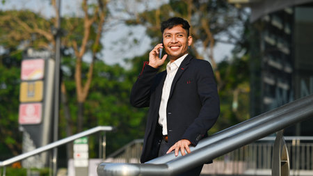 Handsome businessman talking on mobile phone while standing outdoor with cityscape background in...