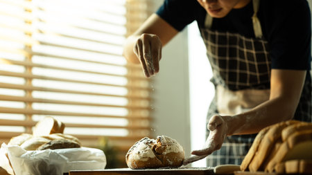 Concentrated male baker sprinkling flour on dough, prepares bread in kitchen.の写真素材
