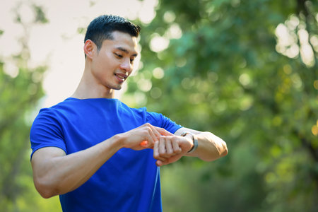 Handsome male runner checking smartwatch to monitor training results. Technology health, wellness concept.の写真素材