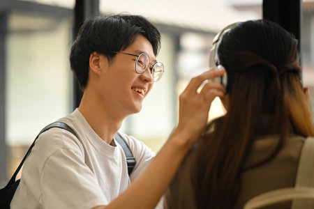 Happy moment of loving young asian man wearing headphones to his girlfriend. Lifestyle and love concept.の写真素材