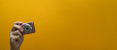 Unrecognizable hand holding old compact camera over yellow background with copy space.