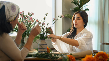 Pretty young asian woman and her senior mother making a bouquet with fresh flowers at floral shop....