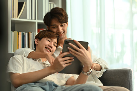 Passionate young gay couple relaxing on couch and browsing internet on digital tablet. LGBT, love and lifestyle concept.の写真素材