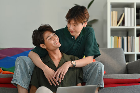 Romantic happy gay couple embracing and using laptop in living room. LGBT, love and lifestyle...