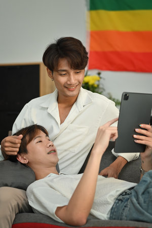 Loving homosexual couple embracing and using digital tablet on couch. LGBT, love and lifestyle relationship concept.の写真素材