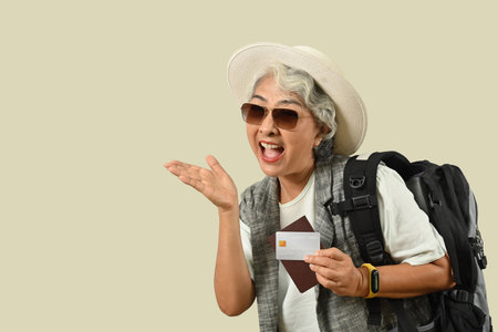Smiling mature female traveler with backpack holding credit card and pointing at copy space, ready for summer vacation, journey trip.の写真素材