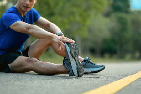 Shot of active sportsman in fitness clothes stretching leg, preparing for morning workout in the public park.の写真素材