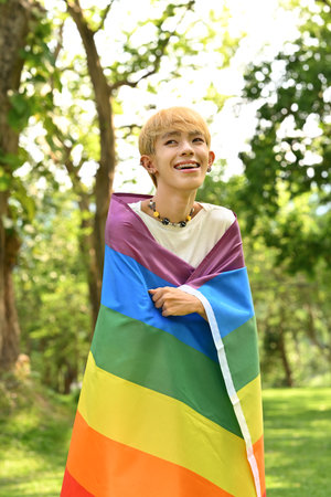 Portrait of happy smiling young man wrapped in a pride rainbow flag. LGBTQ community, freedom, solidarity and equal rights.の写真素材