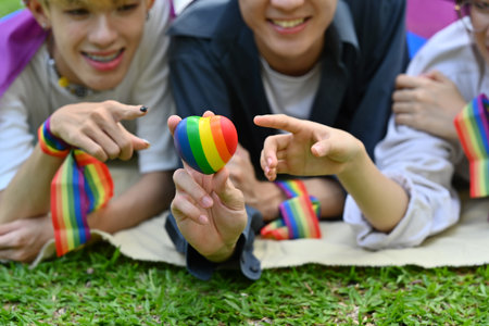 Group of young people wearing rainbow awareness wristbands, enjoying outdoor activities at public park. LGBTQ community concept.の写真素材