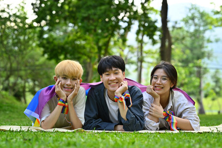 Group of young people wearing rainbow awareness wristbands, enjoying outdoor activities at public park. LGBTQ community concept.の写真素材