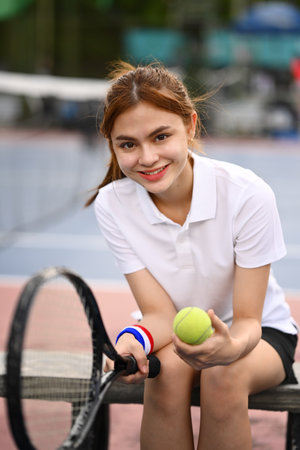 Portrait of female tennis player with racket and ball resting on the bench at the tennis court.の写真素材