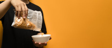 Cropped shot of man pouring cereals into a white bowl isolated on yellow background with space for...