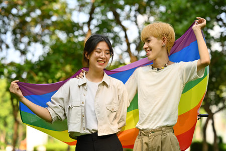 Male and female LGBT friends holding and raising a rainbow flag, supporting LGBTQ community and equality social.の写真素材