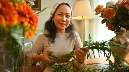 Beautiful senior woman making a bouquet with fresh flowers at floral shop. Small business concept.