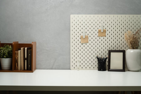 Stylish workplace with books, picture frame, pencil holder and pegboard on wall.