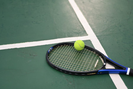A tennis racket and ball on green floor of the court with sunlight. Outdoor sports and healthy lifestyle concept.の写真素材