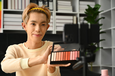 Young male influencer recording video blog about new cosmetic products at home. LGBTQ, blogging, makeup and lifestyle concept.の写真素材