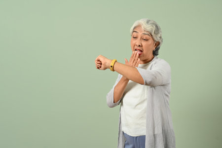 Shocked mature woman checking time on wrist watch isolated on light green background.の写真素材