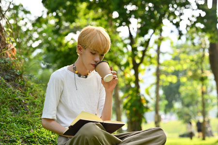 Carefree stylish man relaxing under a tree and reading book on cloudy autumn day. University,...