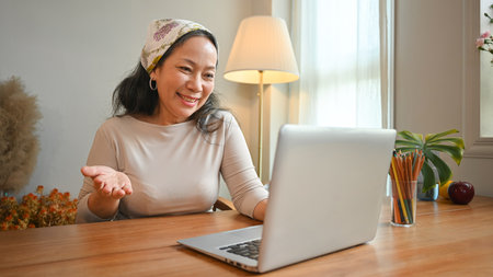 Smiling middle age woman making video call with family or friends on laptop. People, technology and...