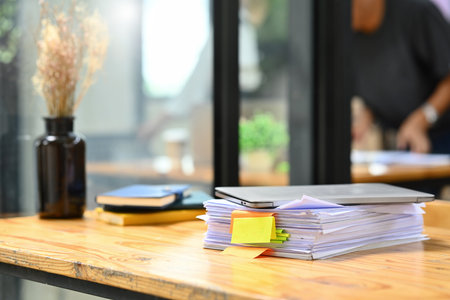 Wooden office desk with pile of documents, laptop and supplies.の写真素材