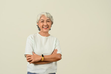 Positive gray haired senior woman standing with arms crossed over green pastel background.の写真素材
