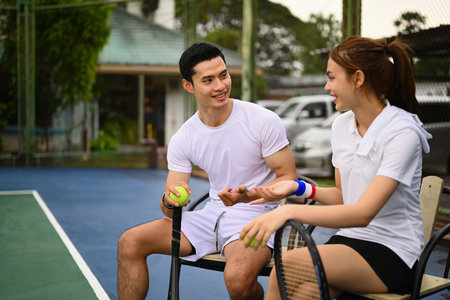 Male and female tennis players talking and resting after game. Sport activity, tennis training and competition concept.の写真素材