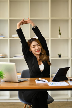 Relaxed office worker woman stretching arms, taking break from work on laptop. Fatigue relieve at workplace concept.の写真素材