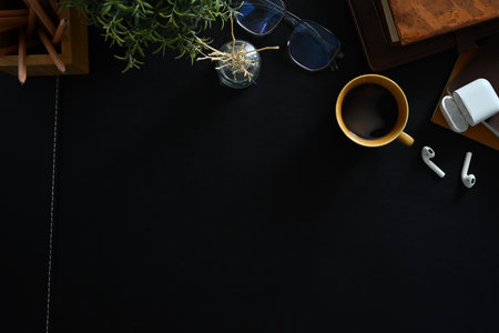 Above view of stylish workplace with cup of coffee, glasses notebook and earphones on black leather background.の写真素材