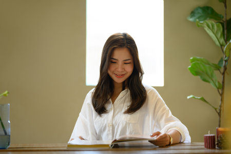 Serene asian woman in casual clothes reading novel in cozy home interior. People, leisure and...