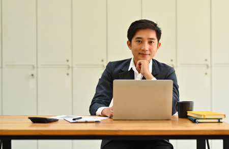 Portrait of successful businessman sitting informs of laptop in modern office and smiling to camera.の写真素材