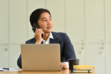 Handsome millennial business executive having phone conversation and looking away. Business, technology and communication.の写真素材
