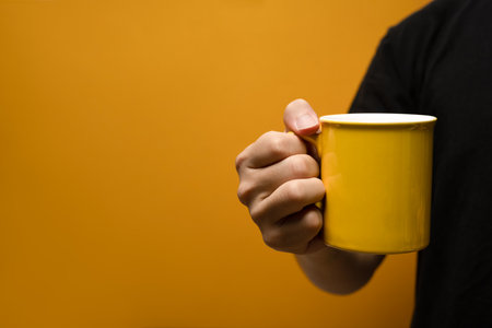 Man holding coffee cup over yellow background. Close up, mockup image, copy space for text.の写真素材