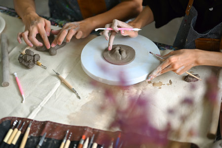 Man hands shaping and scraping raw clay on pottery wheel, creating handmade ceramics in art class.の写真素材