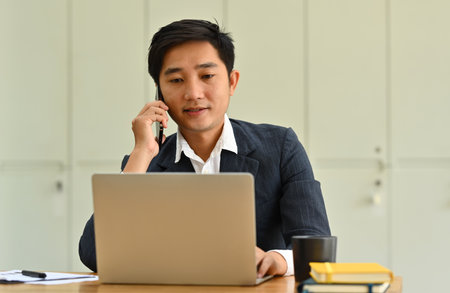Attractive millennial entrepreneur using laptop and talking to business partners at modern workplace.の写真素材