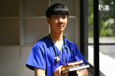 Young male medical students wearing blue scrubs with stethoscope standing near window in sunny day...