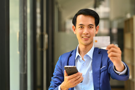 Happy businessman holding credit card and using smartphone, e-commerce, online shopping and financial transaction.の写真素材