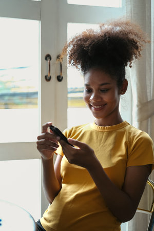 Charming African American woman checking social media, chatting on smartphone. Technology,...