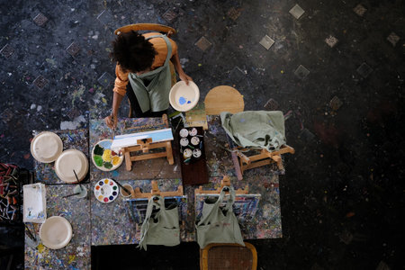 Aerial view of skilled female student painting picture on canvas in dark creative studio. Art, education and creative hobby concept.の写真素材