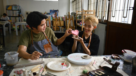 Happy asian gay couple enjoying creative process, creating handmade ceramics in art class. LGBTQ,...