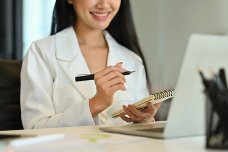 Young businesswoman watching online webinar and writing important information on notebook.の写真素材