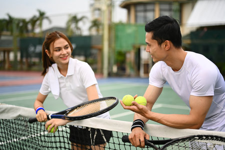 Experienced male tennis coach giving instructions to his student, standing by net at the outdoor tennis court.の写真素材